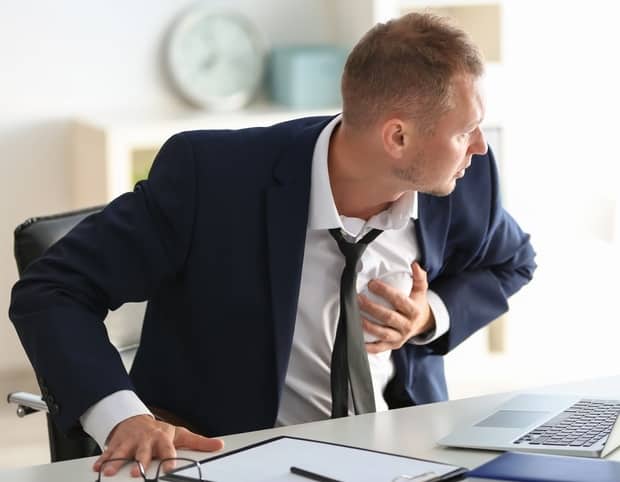 Diagnosis of panic attacks. The picture shows a man during panic attack sitting on the desk with hand on his chest 